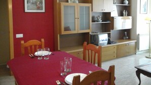 A dining area with a red tablecloth, wooden chairs, a television, and a cabinet with shelves. - Apartment Fira HUTB-014228 (L'Hospitalet de Llobregat)