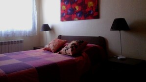 A bedroom with a bed, two bedside lamps, a radiator, and a colorful abstract painting on the wall. - Apartment Fira HUTB-014228 (L'Hospitalet de Llobregat)