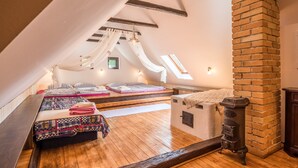 A cozy attic bedroom with a sloped ceiling, exposed wooden beams, a brick chimney, and a skylight. - Country house Fort Lacnov (Lipovce)