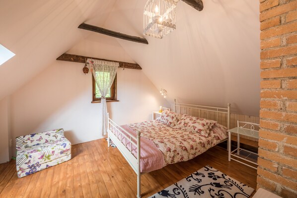 A cozy attic bedroom with a sloped ceiling, a wooden bench, a bed with floral bedding, a small table, and a hanging light fixture.