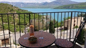 A balcony with a table, a bottle of wine, and a bowl of olives. - Lou Marcelou - Apartment One (Sainte-Croix-du-Verdon)