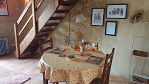 A dining table set with plates, glasses, and a bottle, surrounded by chairs, in a room with a stone wall and a wooden staircase. - Lou Marcelou - Apartment One (Sainte-Croix-du-Verdon)