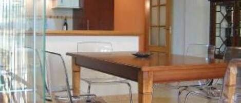 A modern kitchen with wooden cabinets, a dining table with metal chairs, and a pendant light.