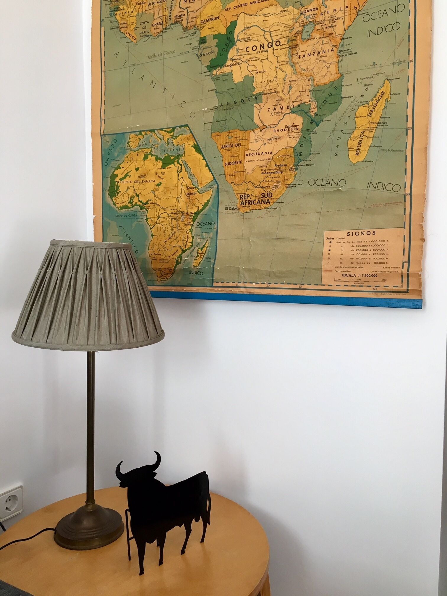 Une carte de l’Afrique et de l’Amérique du Sud est accrochée au mur, avec une lampe et une figurine de vache noire posée sur une table.
