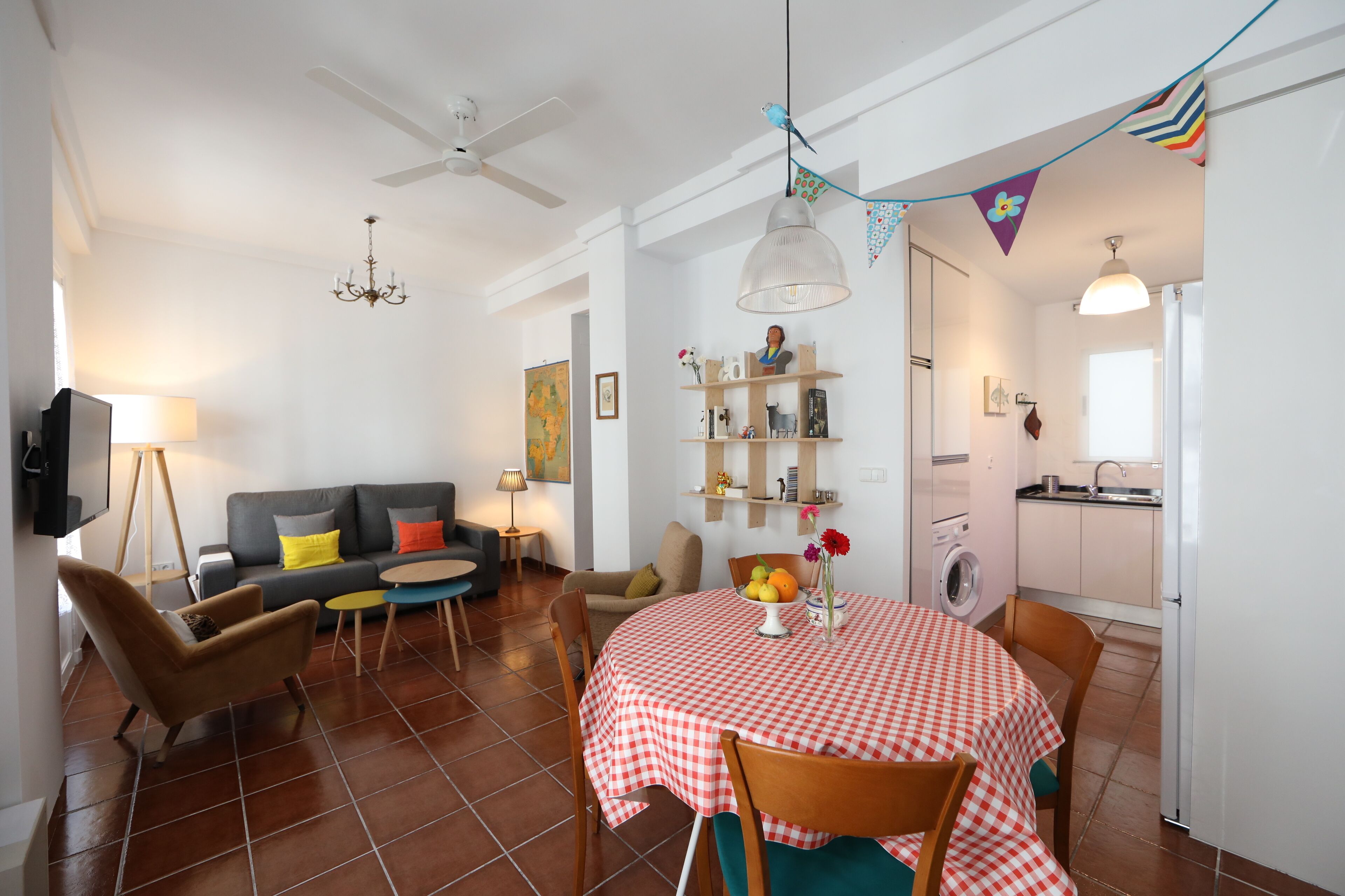 A living room with a sofa, chairs, a dining table with a checkered tablecloth, a chandelier, and a ceiling fan.