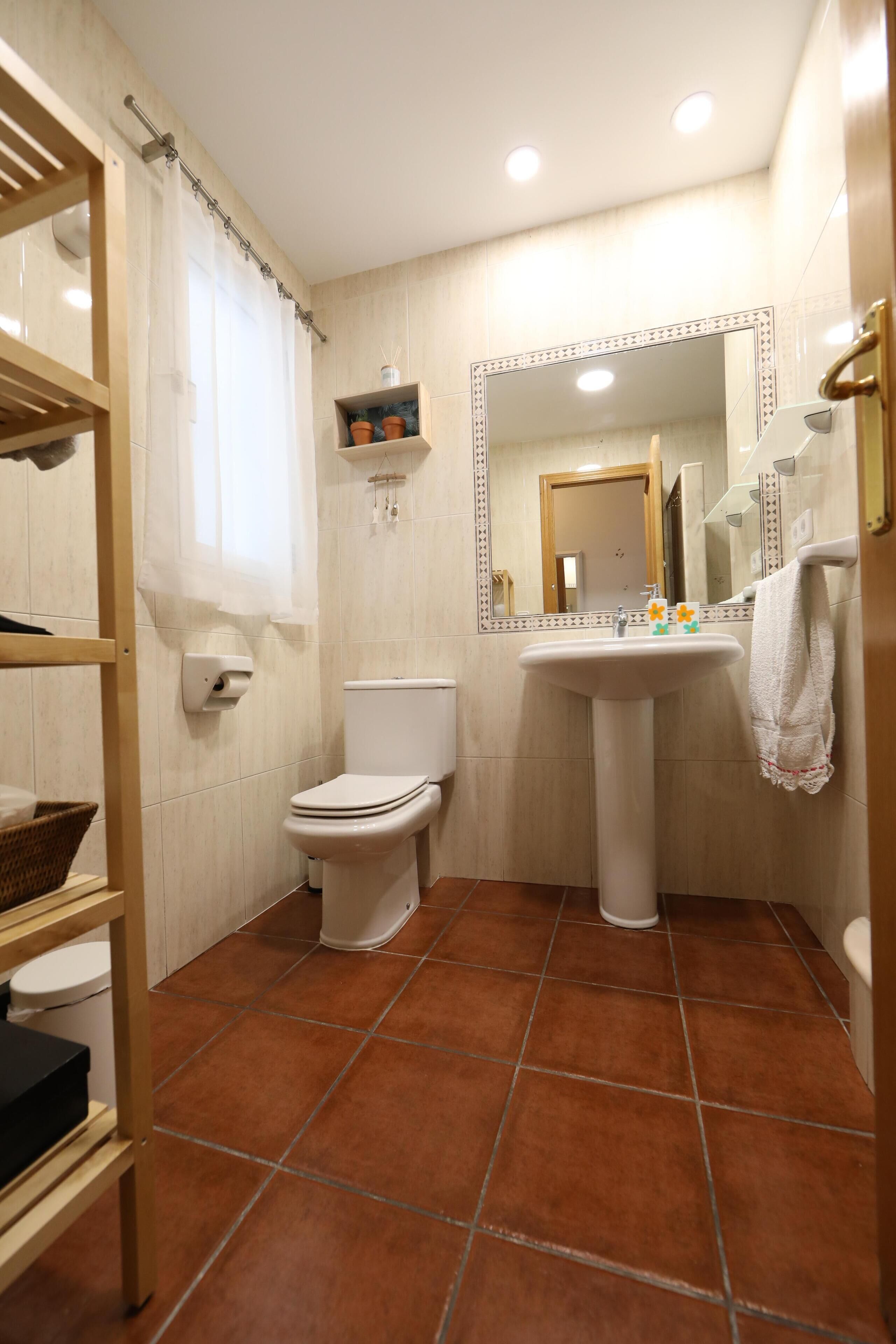 A bathroom with a toilet, sink, mirror, and tiled floor.