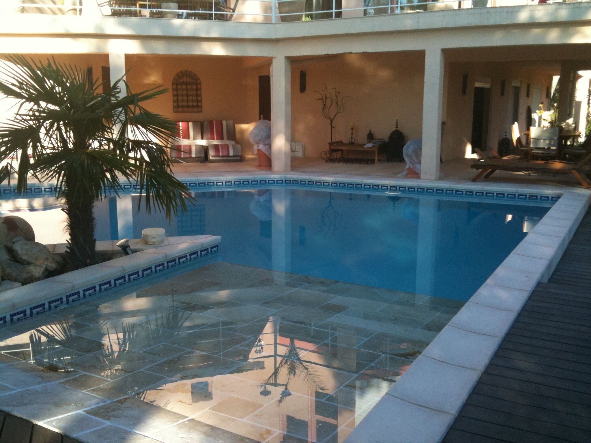 A pool area with a tiled floor, a palm tree, and a lounge chair.