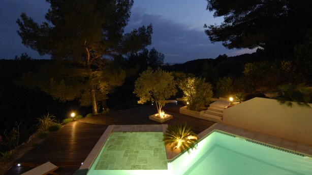 A swimming pool with a wooden deck, surrounded by trees and night lighting. - Nice architect house with stunning pine view only 4km from Aix en Provence (Saint-Marc-Jaumegarde)