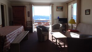 Een kamer met een bed, een bureau, een stoel, een bank, een televisie en uitzicht op de bergen.