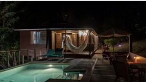 Un espace aménagé au bord de la piscine, avec un hamac, des chaises et une table placés sous un auvent.