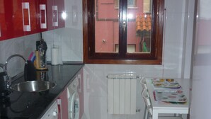 Una cucina compatta con mobili rossi, una lavatrice, un termosifone e un tavolo da pranzo con un libro per bambini.