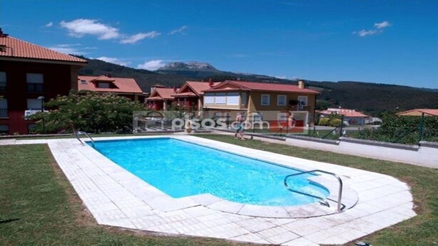 Una piscina con bordo piastrellato, circondata da edifici con tetti rossi e uno sfondo montuoso.