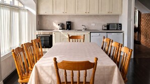 A dining area with a long table, wooden chairs, a kitchen with cabinets, a microwave, and a coffee maker. - Aran View Holiday Homes Doolin - The Courtyard House - Sleeps 9 (Doolin)