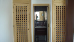 A narrow hallway with wooden lattice doors leading to a bathroom with a tiled backsplash and a mirror.