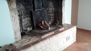 A fireplace with a stone mantle, a metal grate, and logs burning. - Holidays House, NORMANDY, Gite in the marshes of Carentan -wifi (Terre-Et-Marais)