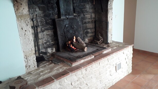 A fireplace with a stone mantle, a metal grate, and logs burning. - Holidays House, NORMANDY, Gite in the marshes of Carentan -wifi (Terre-Et-Marais)