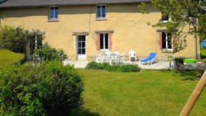 A two-story house with a flat roof, a front porch with a table and chairs, and a small garden area. - Holidays House, NORMANDY, Gite in the marshes of Carentan -wifi (Terre-Et-Marais)