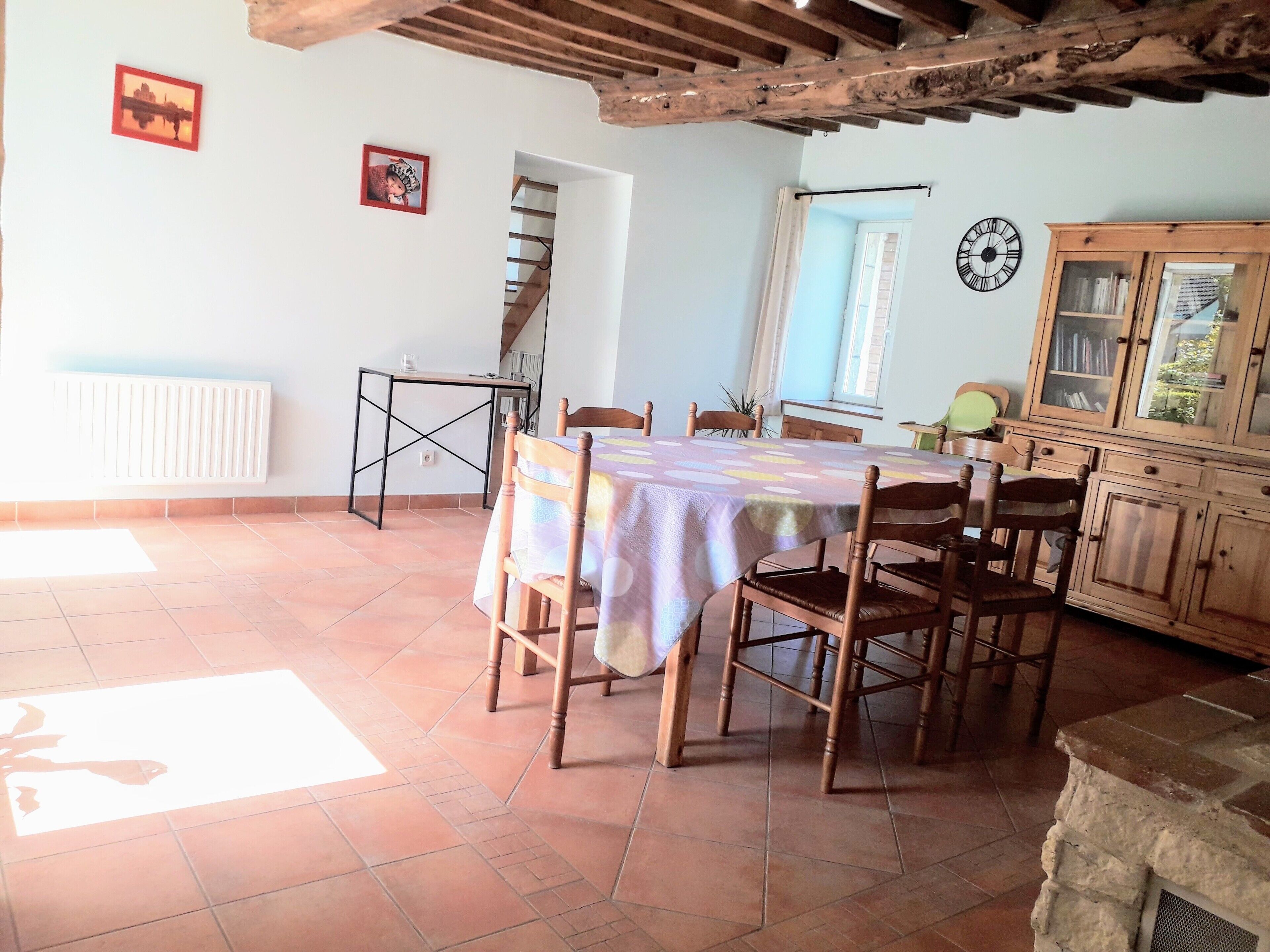 A dining area with a table covered by a patterned tablecloth, surrounded by wooden chairs.