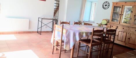 A dining area with a table covered by a patterned tablecloth, surrounded by wooden chairs.