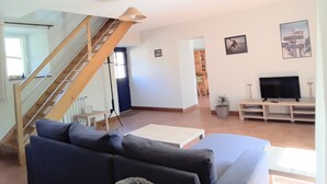 A living room with a staircase, a sofa, a TV, and a plant. - Holidays House, NORMANDY, Gite in the marshes of Carentan -wifi (Terre-Et-Marais)