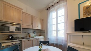 A compact kitchen with wooden cabinets, a built-in oven, a sink, and a dining area with a table and chairs. - Studio in the heart of Finalborgo (Finale Ligure)