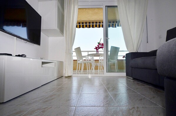 A modern living room with a flat-screen TV, a sofa, and a balcony with chairs and a table.