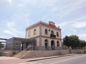 Een gebouw met een bord waarop 'Pineda de Mar' staat, een trap naar een ingang en een persoon die over het trottoir loopt.