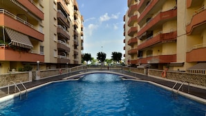 A swimming pool surrounded by multi-story buildings with balconies, a clear sky, and trees in the background. - Spectacular Frontline, Pineda de Mar (Pineda de Mar)