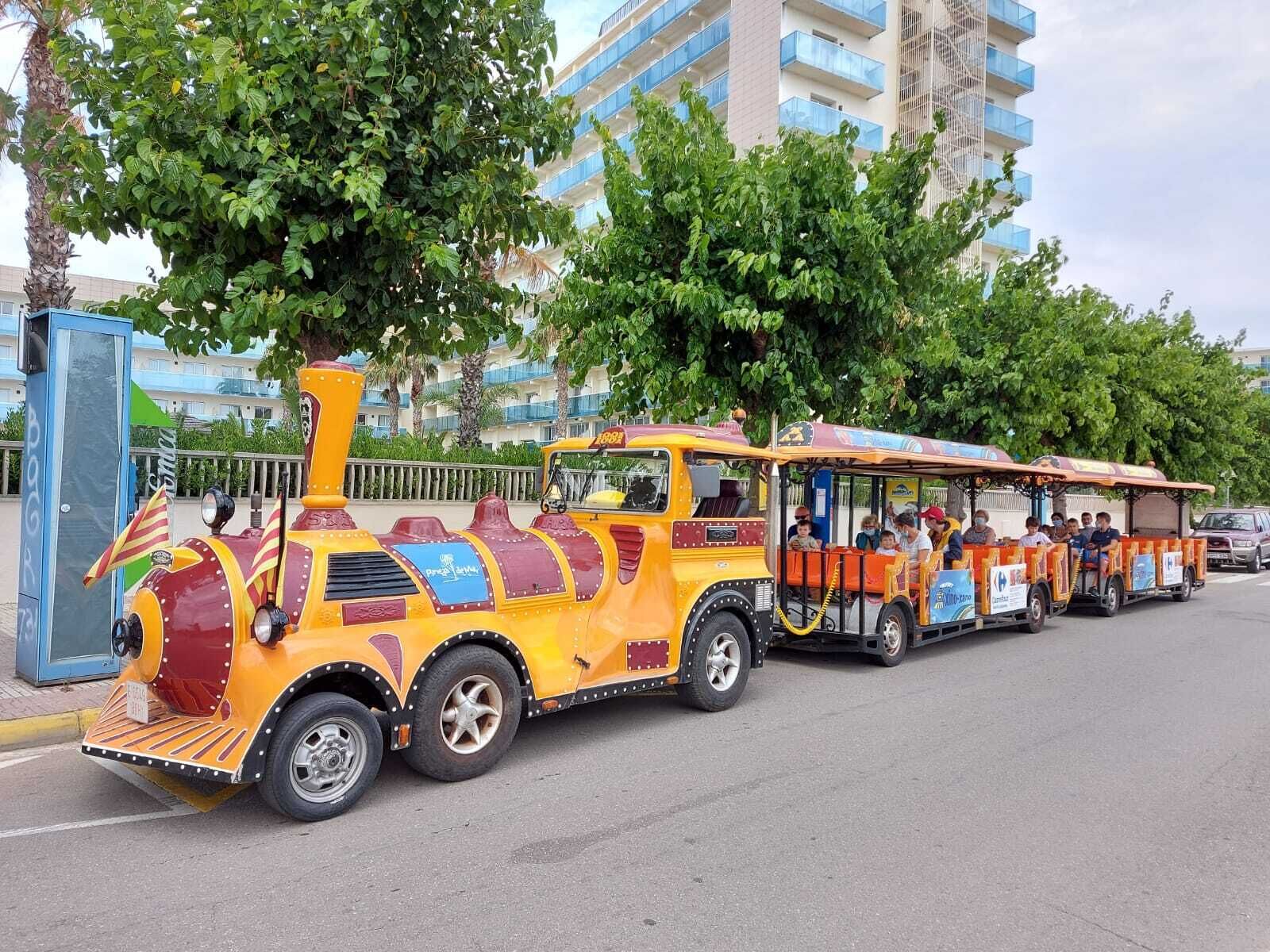 Un autobus aux couleurs vives, décoré sur le thème du train et transportant des passagers, est garé dans une rue, avec des bâtiments et des arbres en arrière-plan.