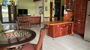 A dining area with a round table, chairs, a wooden island with cabinets, pendant lights, a television, and a door leading to another room. - El Roble: villa directly on the beach. (El Roble)
