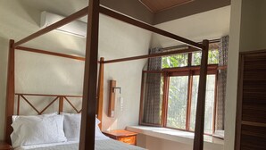 A four-poster bed with a wooden frame, a bedside table, a window with a view of greenery, and a wall-mounted light fixture. - El Roble: villa directly on the beach. (El Roble)