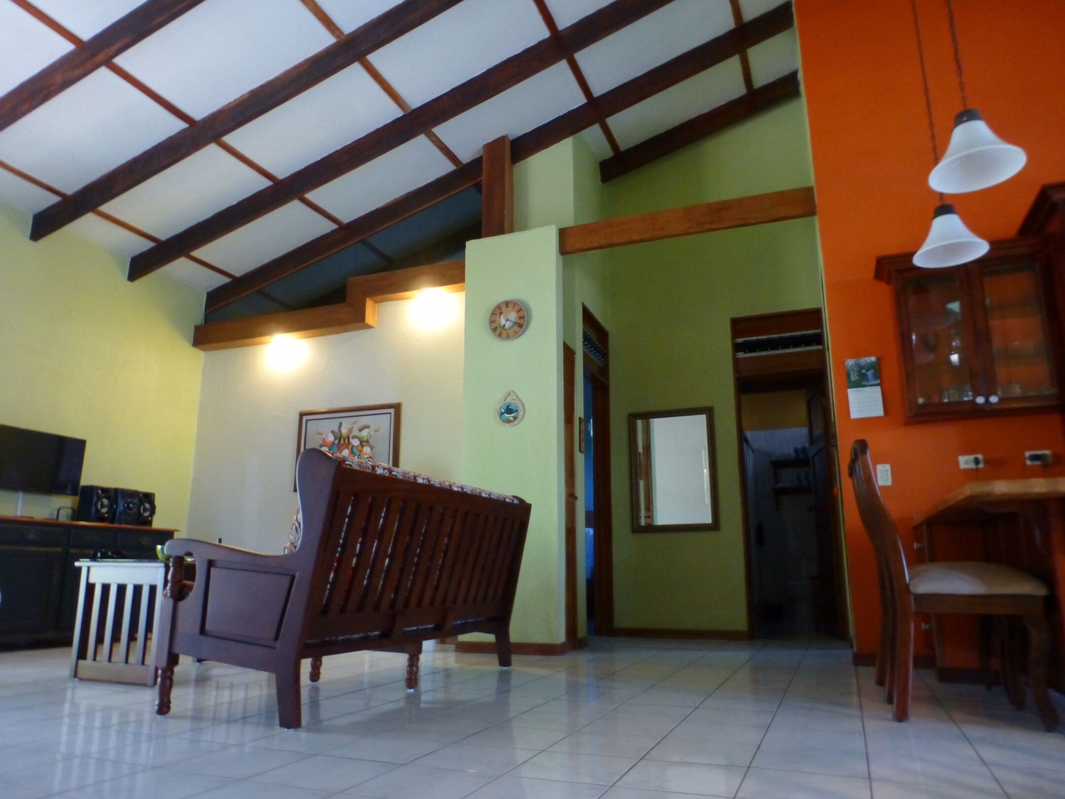 Un salón amplio con techo alto, un banco de madera, una zona de comedor con sillas y un televisor.