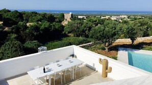 Una terraza en la azotea con zona de comedor, piscina y vistas al mar y al paisaje circundante.