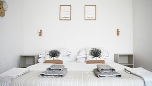 Una cama bien hecha con dos almohadas, una mesita de noche y una pared con dos citas inspiradoras enmarcadas.
