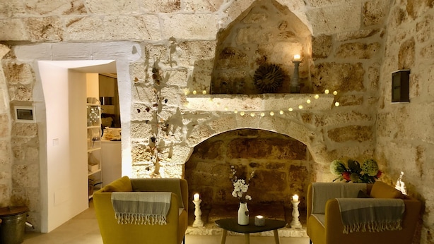 Una habitación acogedora con paredes de piedra, una chimenea, dos sillones amarillos y una pequeña mesa con velas.