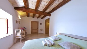 Un dormitorio con cama, una silla, una mesa con flores y una puerta que da a otra habitación.