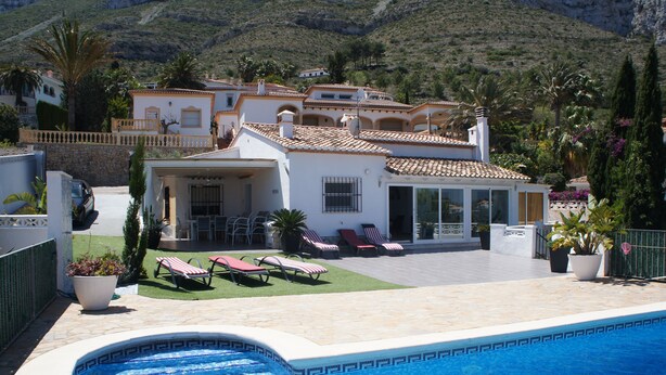 A poolside view of a Mediterranean-style villa with a swimming pool, sun loungers, and a patio area. - House with panoramic views towards the sea and mountains  (Dénia)