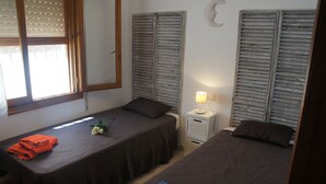 A room with two single beds, a small bedside table with a lamp, a window with blinds, and a mirror on the wall. - House with panoramic views towards the sea and mountains  (Dénia)