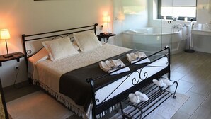 Een netjes opgemaakt bed met kussens en handdoeken, een nachtkastje met een lamp, een groot raam met uitzicht, en een bad in de badkamer.