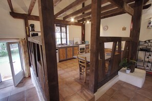 A rustic kitchen with wooden beams, a dining area with a table and chairs, and a view of the outside.