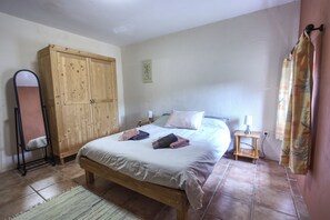 A bedroom with a wooden bed, a wardrobe, a bedside table with a lamp, and a mirror.