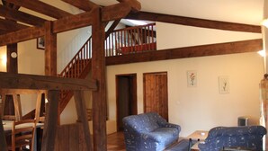A spacious living area with a high ceiling, wooden beams, a staircase, and a sofa. - Le Rosier, Gîtes de Peyrounou. Spacious 2 bedroom gîte. (Lacapelle Biron)
