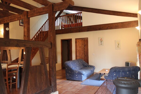 A spacious living area with a high ceiling, wooden beams, a staircase, and a sofa.