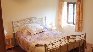 A bedroom with a bed, a nightstand, a chair, a window with curtains, and a hanging light fixture. - Le Rosier, Gîtes de Peyrounou. Spacious 2 bedroom gîte. (Lacapelle Biron)