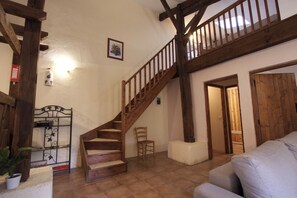 A spacious living area with a wooden staircase leading to an upper level, a white wall with a framed picture, and a door leading to another room.