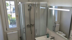 Ett modernt badrum med en duschkabin i glas, en toalett, ett handfat med spegel och en tvättmaskin.