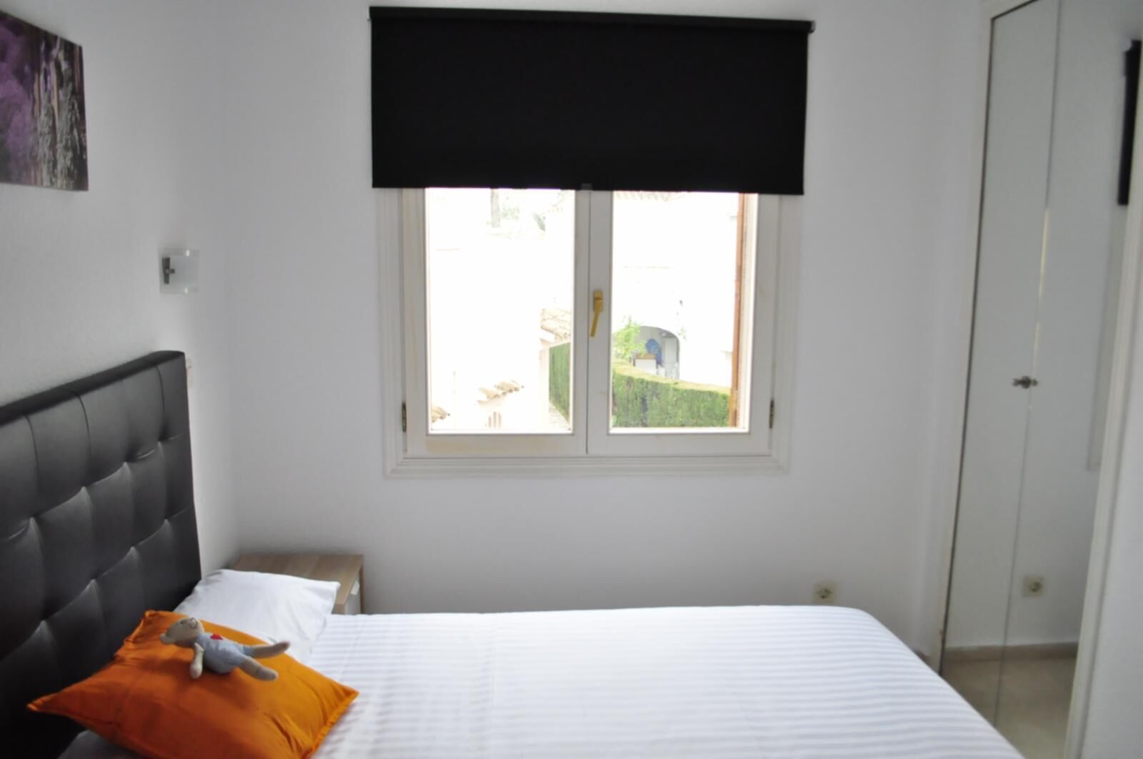 Una camera da letto con un letto, un comodino, una finestra dotata di persiana nera e una porta.