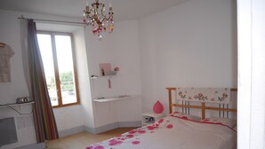 A bedroom with a bed, a desk, a chair, a window, and a chandelier.