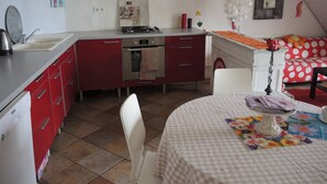 A kitchen with red cabinets, a gas stove, and a sink. There is a dining table with a floral tablecloth and a chair.