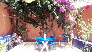 A patio with a blue table and chairs, surrounded by potted plants and flowering vines on a wall. - Aourir: House / Villa - Aourir (Aourir)